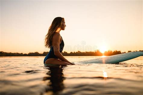 Side View Of Beautiful Woman Sitting On Surf Style Wakeboard On Water