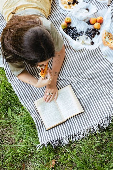 Brunette Woman Reading Book And Eating Pizza In Park By Stocksy
