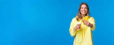 Fröhliche hübsche feminine blonde kurzhaarige Frau in gelbem Hoodie sich mit Kaffee zum