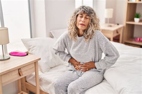 Middle Age Woman Suffering For Menstrual Pain Sitting On Bed At Bedroom