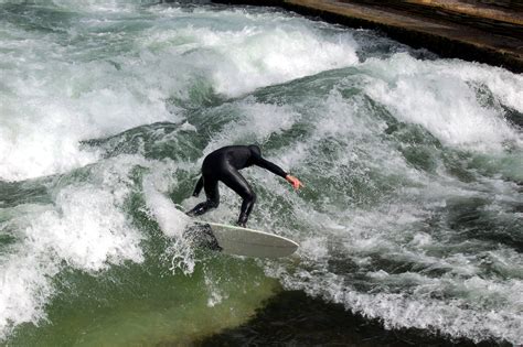 Surfer On The White Surfboard On The Green Eisbach River In Munich