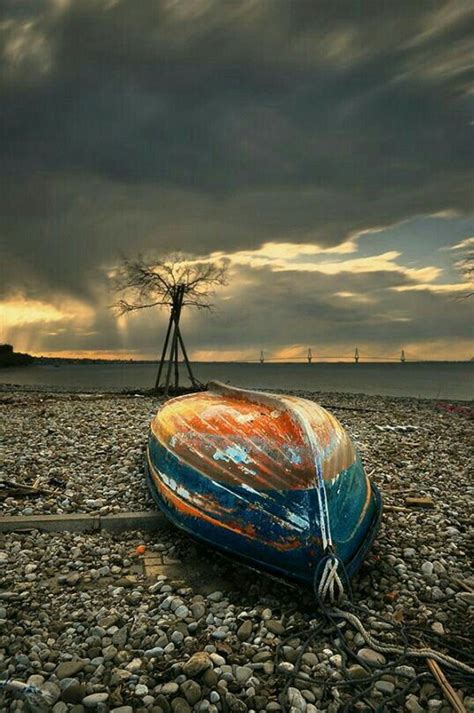 An Old Boat Is Sitting On The Beach With Rocks Under It And A Windmill