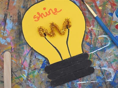 A Yellow Light Bulb With Some Gold Flowers In It And Paintbrushes Next