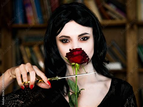 Beautiful Brunette Girl Cosplay Morticia Addams With Red Lips And Nails Holding Red Rose And