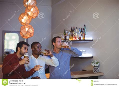 Tres Amigos Que Beben La Cerveza Mientras Que Mira El Partido Imagen De