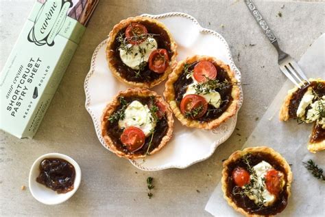 four small pies with tomatoes and cheese on top, next to a box of crackers