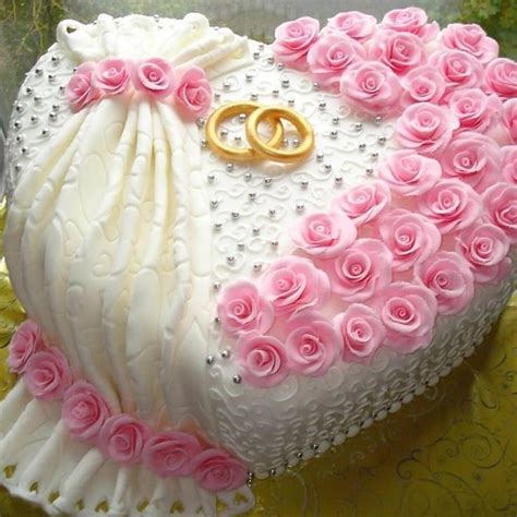 A Heart Shaped Cake Decorated With Pink Roses And Two Gold Wedding Rings