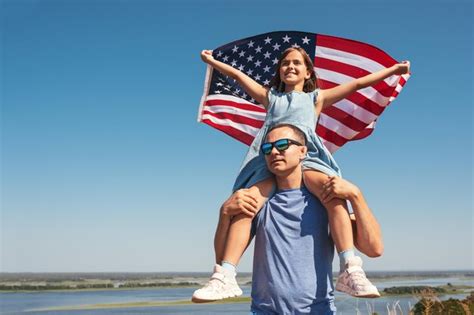 Niña feliz se sienta sobre los hombros de su padre con la bandera de