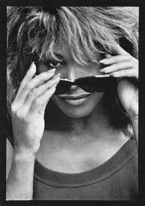 A Black And White Photo Of A Woman Holding Her Sunglasses Up To Her