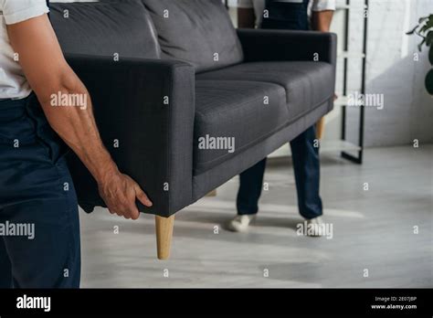 Partial View Of Workers Carrying Heavy Sofa In Apartment Stock Photo