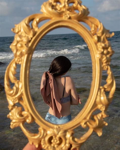 A Woman Standing In Front Of The Ocean Looking At Her Reflection In A