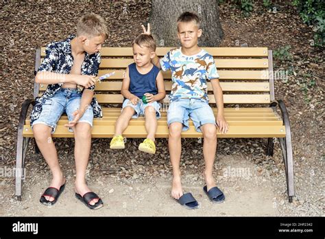 Ältere Brüder Verspotten Den Jüngeren Jungen Der Auf Einer Holzbank Sitzt Vorschulkinder