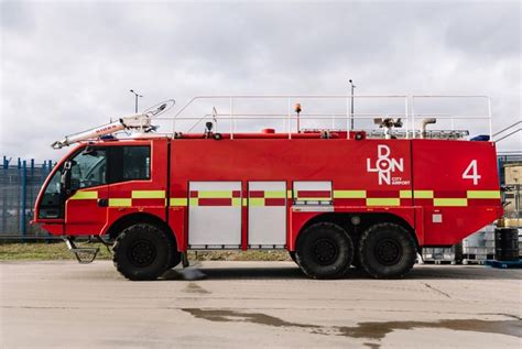 a large red fire truck parked on top of a cement lot next to a building