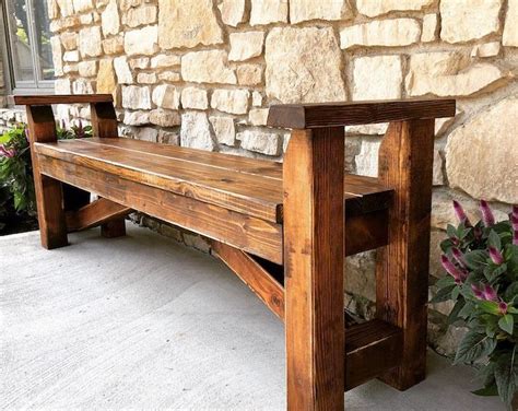 a wooden bench sitting in front of a stone wall with purple flowers on the side