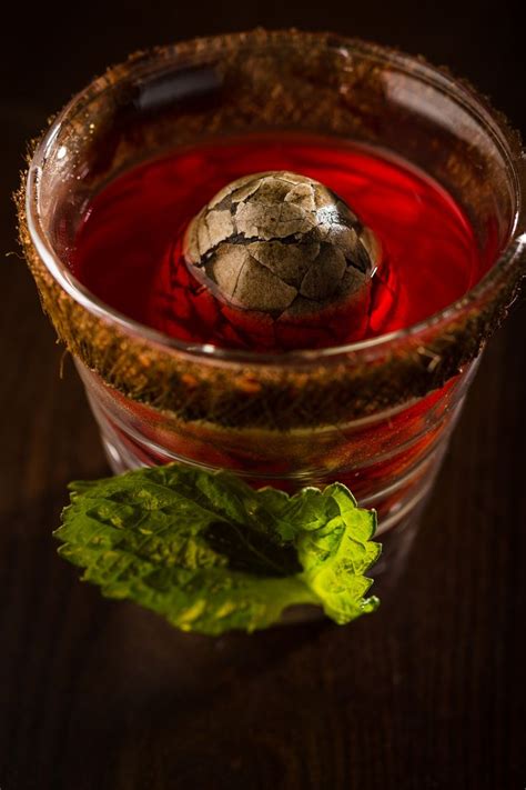 A Close Up Of A Glass Cup Filled With Liquid Next To A Leafy Plant