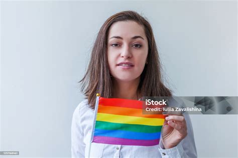 美しい白人のレズビアンの女の子はlgbt虹の旗を持つ幸せで興奮して見える白い背景に隔離されています若い女性ゲイプライドの肖像画lgbtq