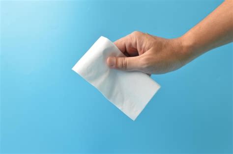 Mano sujetando un pañuelo de papel blanco aislado en un fondo azul