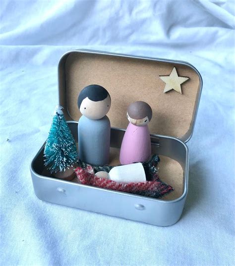 An Open Tin Box With Two Small Wooden Figures In It And A Star On The Top