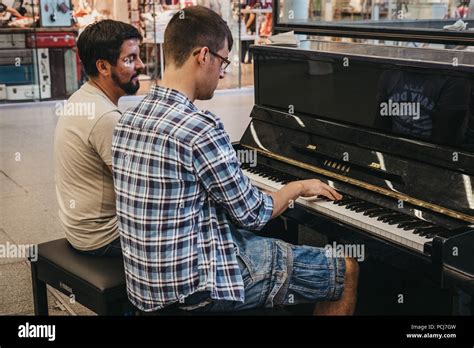 Two man playing a public piano installed in the hall inside St. Pancras ...