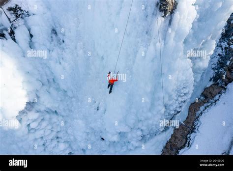 Man Climbing On Frozen Waterfall By Kicking With Crampons Into The Ice