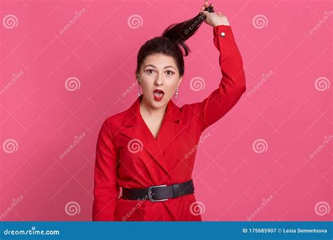 Horizontal Studio Shot Of Emotional Charismatic Brunette Holding Her Ponytail With One Hand