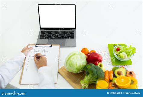 Nutritionist Working On Laptop And Writing Diet Plan For Patient Stock