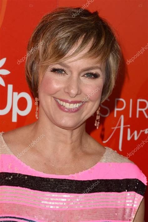 An Older Woman With Short Hair Smiling At The Camera In Front Of A Red