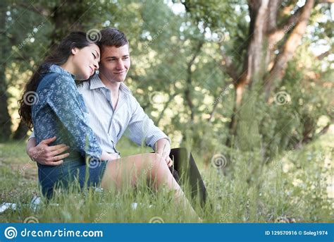 Young Couple Sitting On The Grass In The Forest And Looking On Sunset