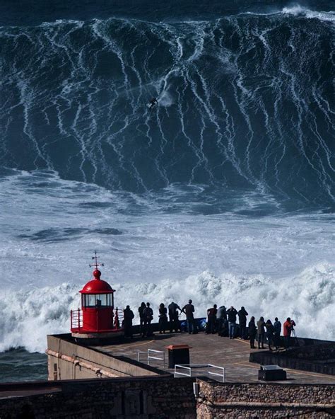 a group of people standing on top of a pier next to a large wave in the ocean