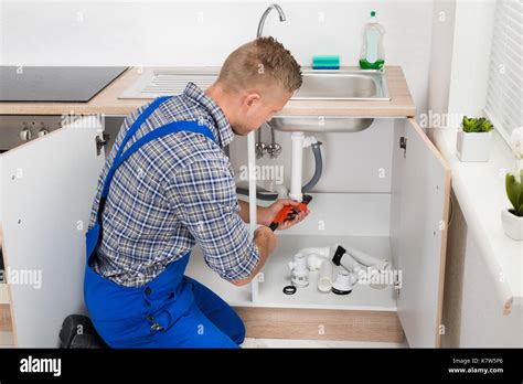 Male Plumber Fixing Sink Pipe With Adjustable Wrench In Kitchen Stock