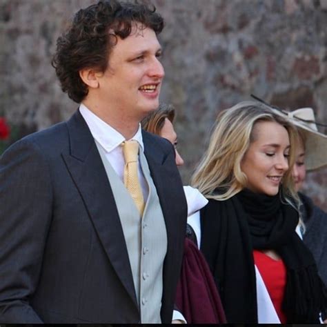 A Man In A Suit And Tie Standing Next To A Woman Wearing A Dress Coat