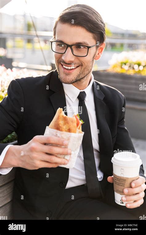 Attractive Smiling Young Businessman Wearing A Suit Sitting On A Bench