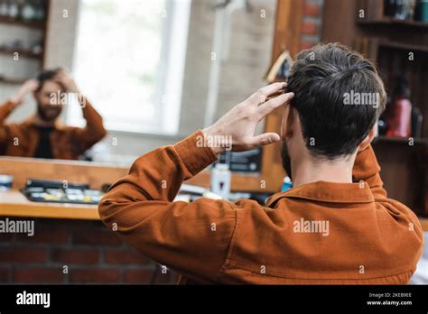 Back View Of Brunette Man Touching Hair While Looking In Blurred Mirror