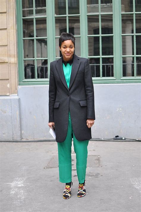 A Woman Wearing Green Pants And A Black Blazer Standing In Front Of A