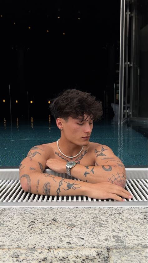 A Man With Tattoos On His Body Sitting Next To A Swimming Pool And Looking At The Camera