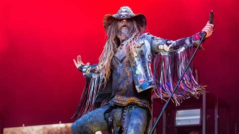 Rob Zombie Is Wearing Blue Dress And Cap In Red Wall Background Hd Rob