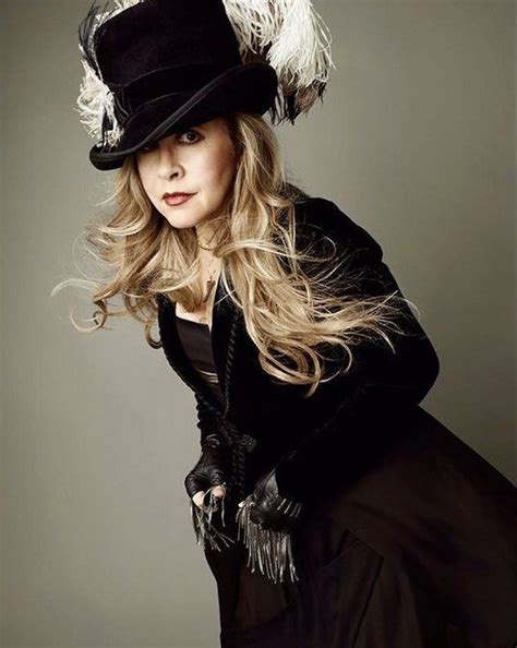 a woman with long hair wearing a black dress and hat, posing for the camera