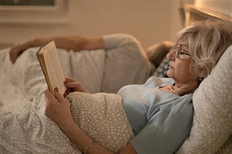 Вид сбоку на зрелую женщину лежащую в постели и читающую книгу ее муж