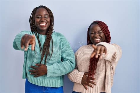 Two African Woman Standing Over Blue Background Laughing At You