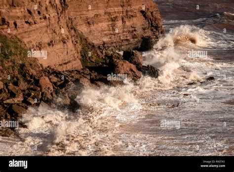 Waves Crashing Into The Red Sandstone Cliffs Of The Jurassic Coast East Devon South West