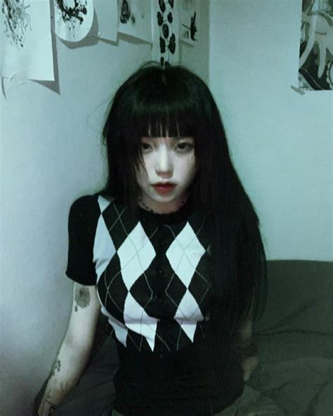 A Woman With Long Black Hair Sitting On Top Of A Bed Next To A Wall