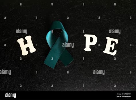 Teal ribbon color isolated on dark black background. Ovarian cancer awareness and hope concept ...