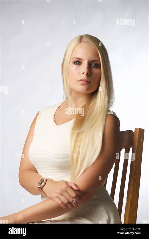 A Blonde Girl Sits On A Chair In The Studio She Wears A White Dress And Is Looking To Camera