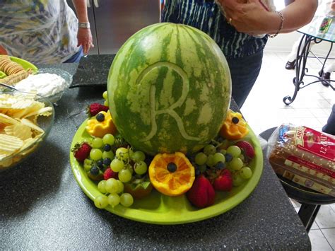 A Watermelon With The Letter R Carved Into It Surrounded By Fruits And Chips