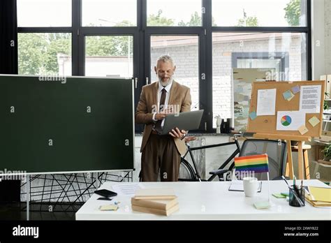 A Mature LGBTQ Teacher With A Beard Uses A Laptop To Teach Online From