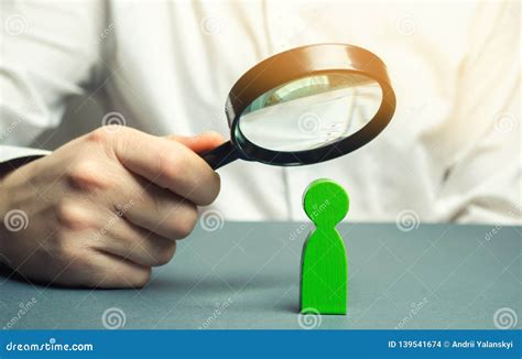 A Businessman Is Holding A Magnifying Glass Over A Green Man Figure