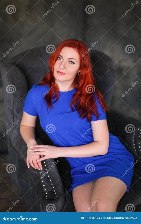 Beautiful Ginger Haired Woman In Blue Dress Sitting In Gray Armchair