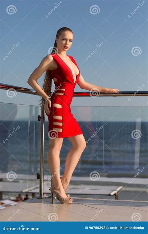 A Woman In A Stunning Red Dress And High Heels On A Hotel`s Balcony On A Blue Sky Background