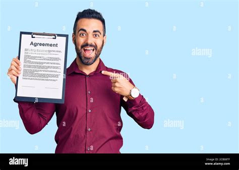 Young Hispanic Man Holding Clipboard With Agreement Document Smiling