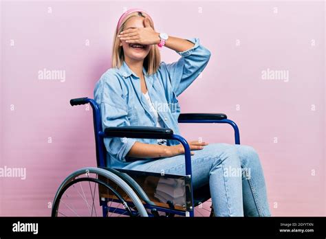 Schöne blonde Frau sitzt auf dem Rollstuhl lächelnd und lachend mit Hand auf Gesicht bedeckende